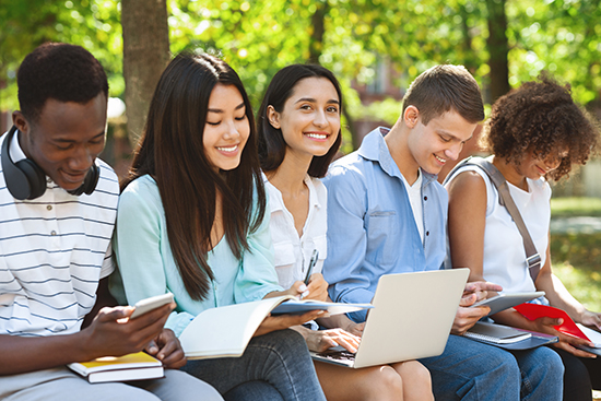 Eine Gruppe internationaler Studierender sitzen draußen. Eine dunkelhaarige schaut in die Kamera und lächelt.