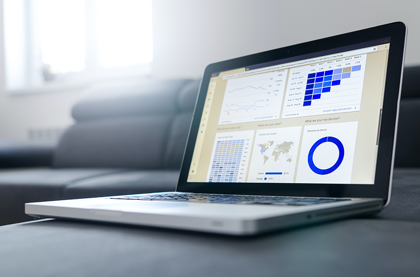 Ein Laptop mit Graphen und Statistiken auf dem Display steht auf einer grauen Couch