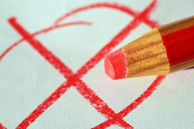 Ein roter Stift liegt auf einem weißen Blatt Papier, auf welches ein mit einem Kreuz durchstrichener Kreis zu sehen ist.