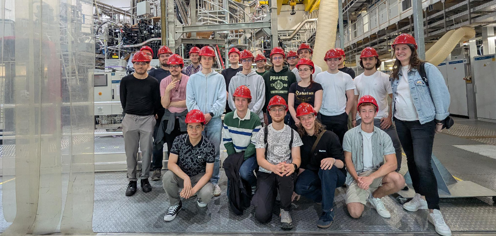 Exkursion Golda Die Exkursions-Gruppe in roten Sicherheitshelmen in einer großen Halle vor einem Plasma-Experiment