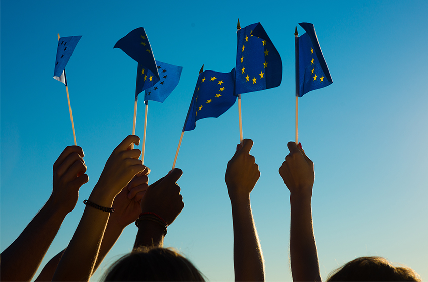 Mehrere Hände wedeln vor einem blauen Abendhimmel mit der europäischen Flagge