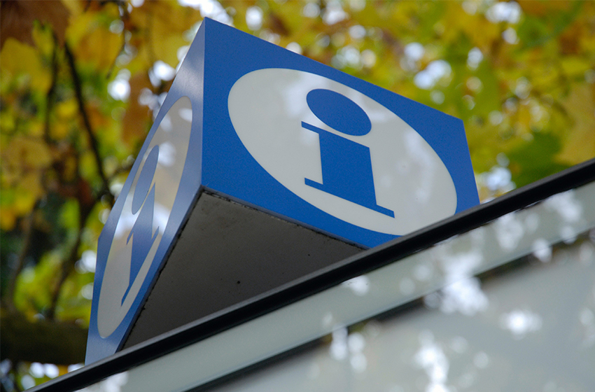 An information sign in the shape of a blue and white cube, photographed from below. Autumn leaves on trees can be seen in the background.