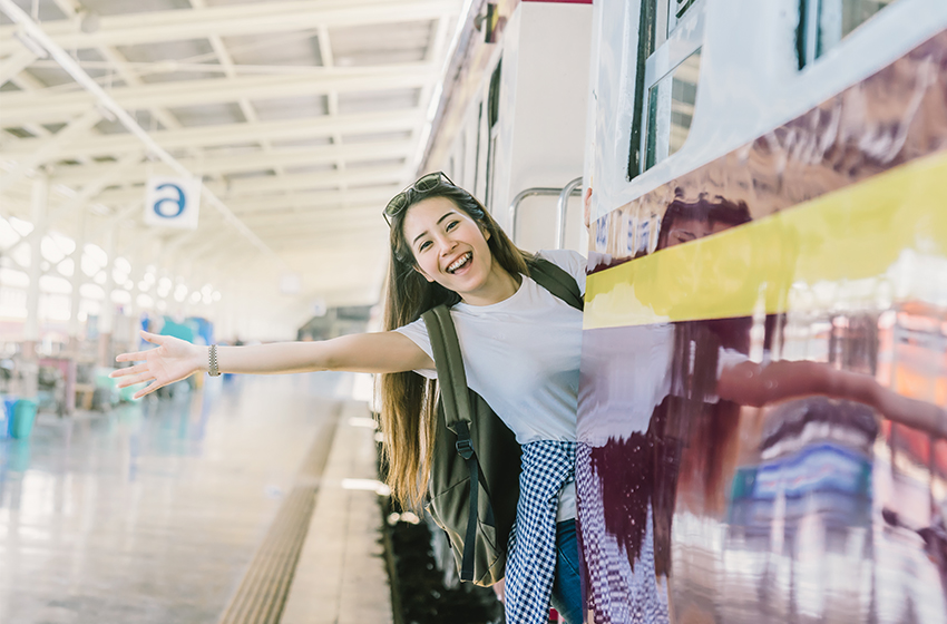 Eine junge Reisende winkt aus einem Zug.