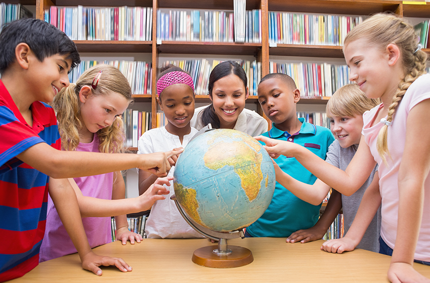 Eine Lehrerin steht mit einer Gruppe Schüler*innen um einen Globus. Die Kinder zeigen auf verschiedene Länder.