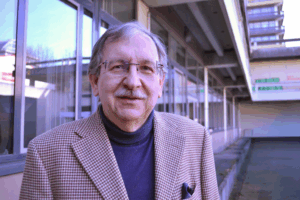 Portrait von Dominik Bomans, ein Herr im braun-karierten Sacko mit eingestecktem Tuch, Brille und Schnauzbart